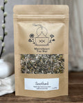 Kraft paper tea bag from Merryheart Tea Hut with visible herbs on a wooden surface.